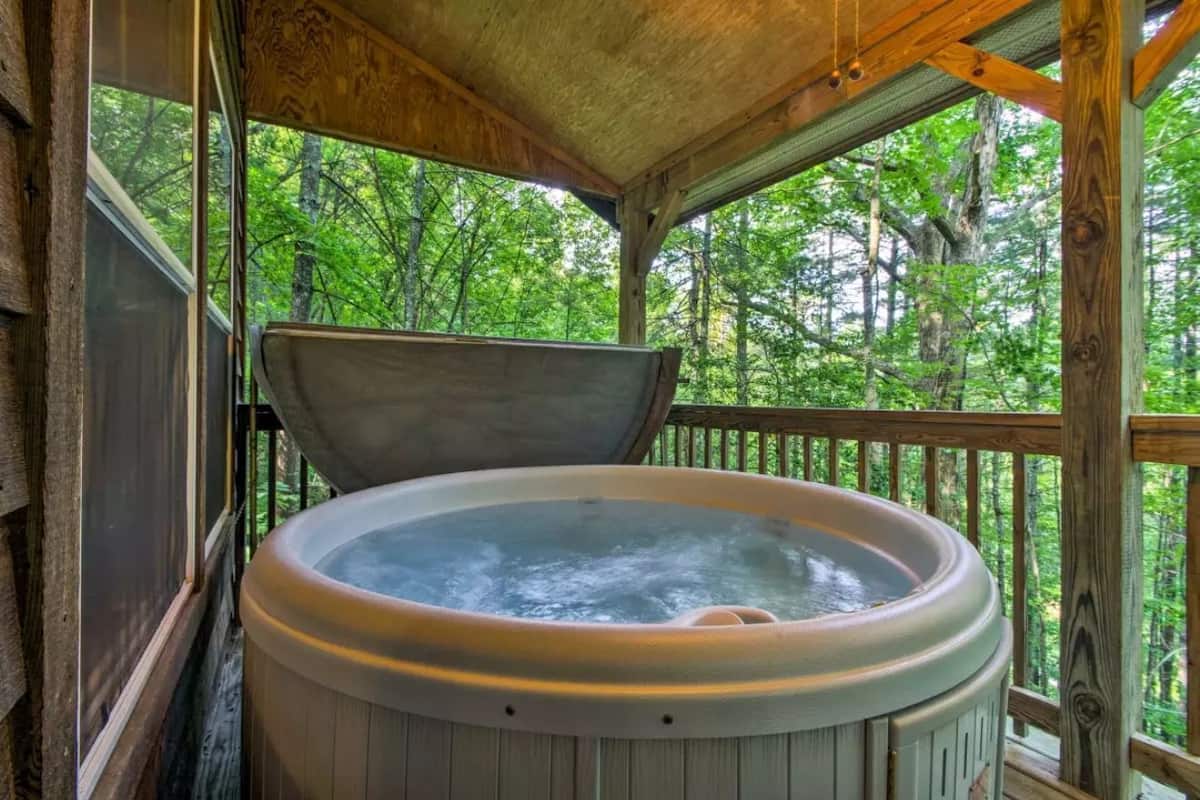 A hot tub in a wooden cabin with a view of a forest.