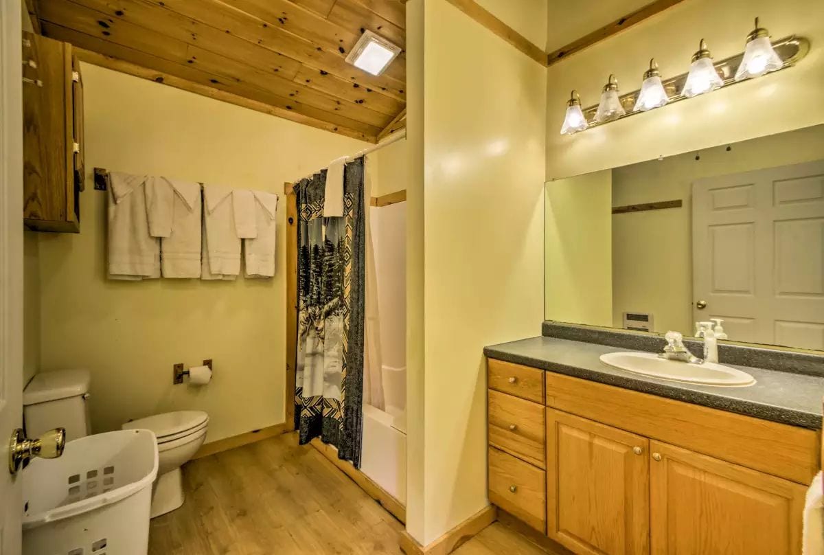 A bathroom with a wooden ceiling, a toilet, a sink, and a shower curtain.
