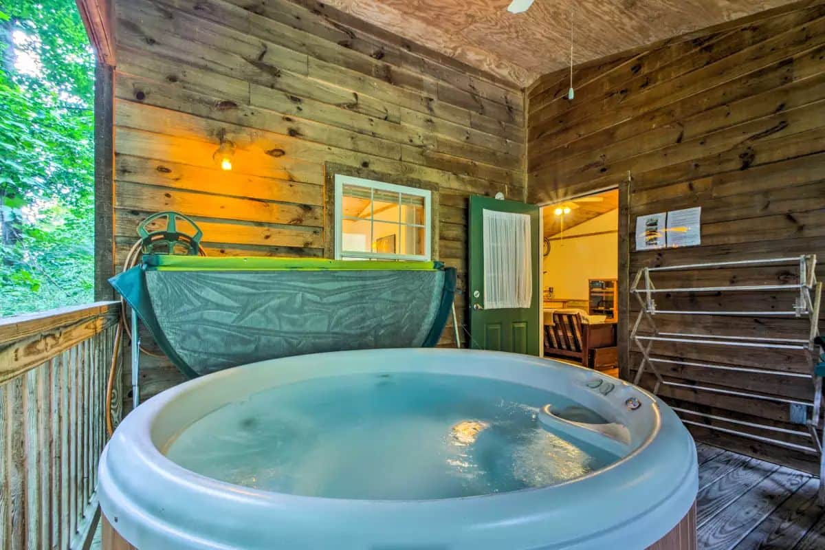 A wooden cabin with a hot tub, a wooden deck, and a view of trees.