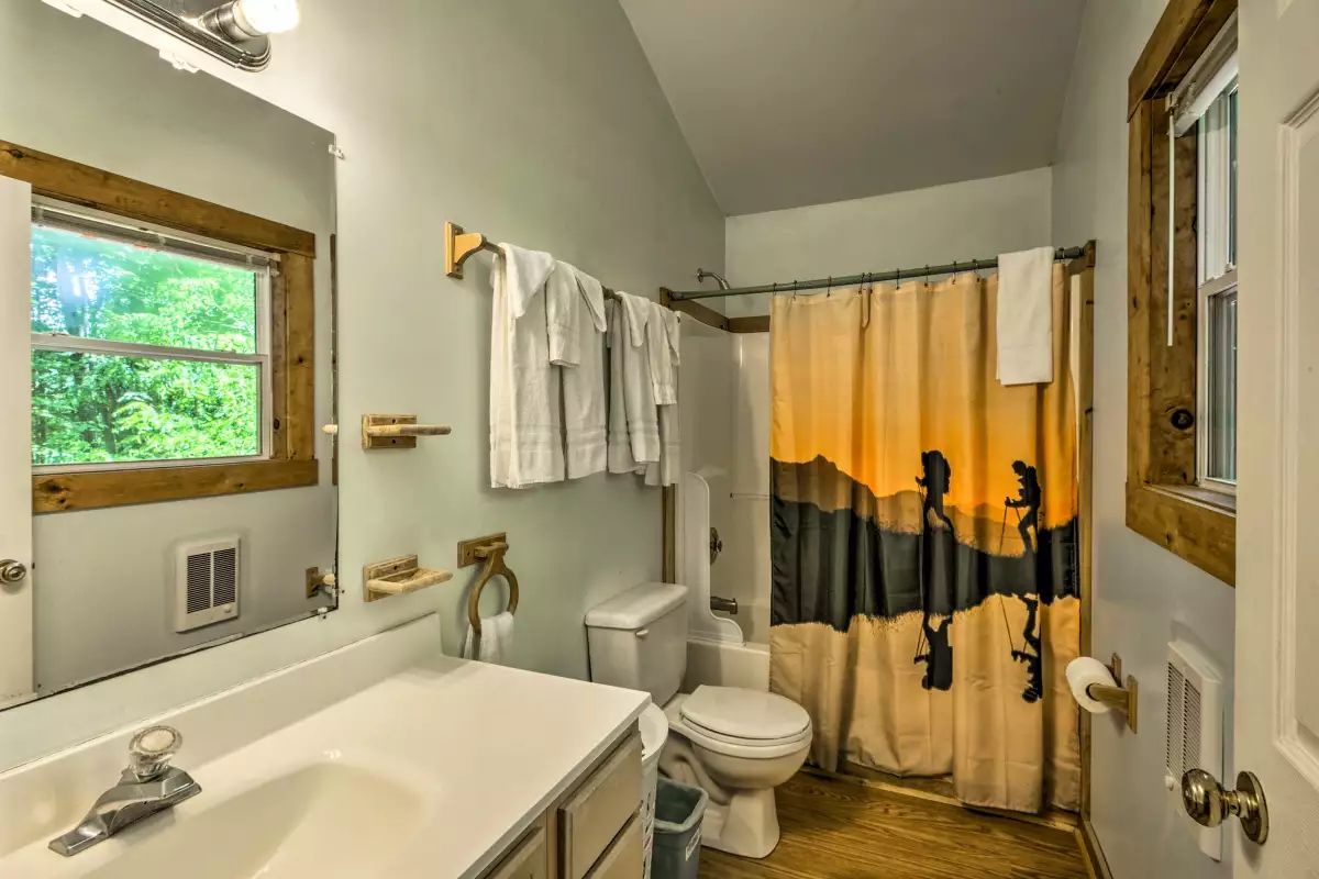 Une salle de bain avec une baignoire, des toilettes et un lavabo. Il y a une fenêtre donnant sur un paysage verdoyant.