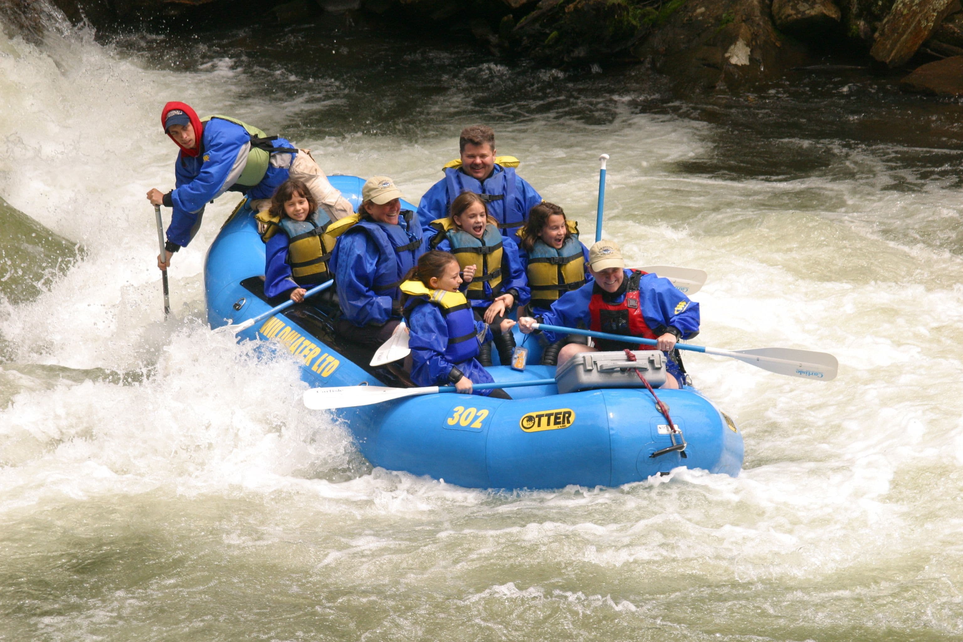 A group of people in a blue raft navigating through a river.