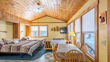 A cabin with two beds, a dining table, chairs, a television, and a window with blinds.