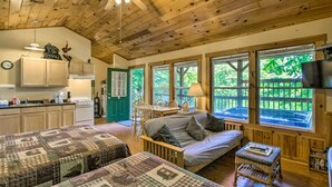 A cozy cabin interior with wooden floors, a dining area, a kitchen, and large windows offering views of the outdoors. - Nantahala Cabins (Bryson City)