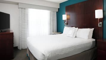 A hotel room with a large bed, a TV, a desk, and a window with curtains.