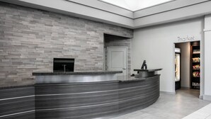 A modern reception area with a curved reception desk, a tiled wall, and a visible entrance to a market area. - Residence Inn by Marriott Lincoln South (Lincoln)