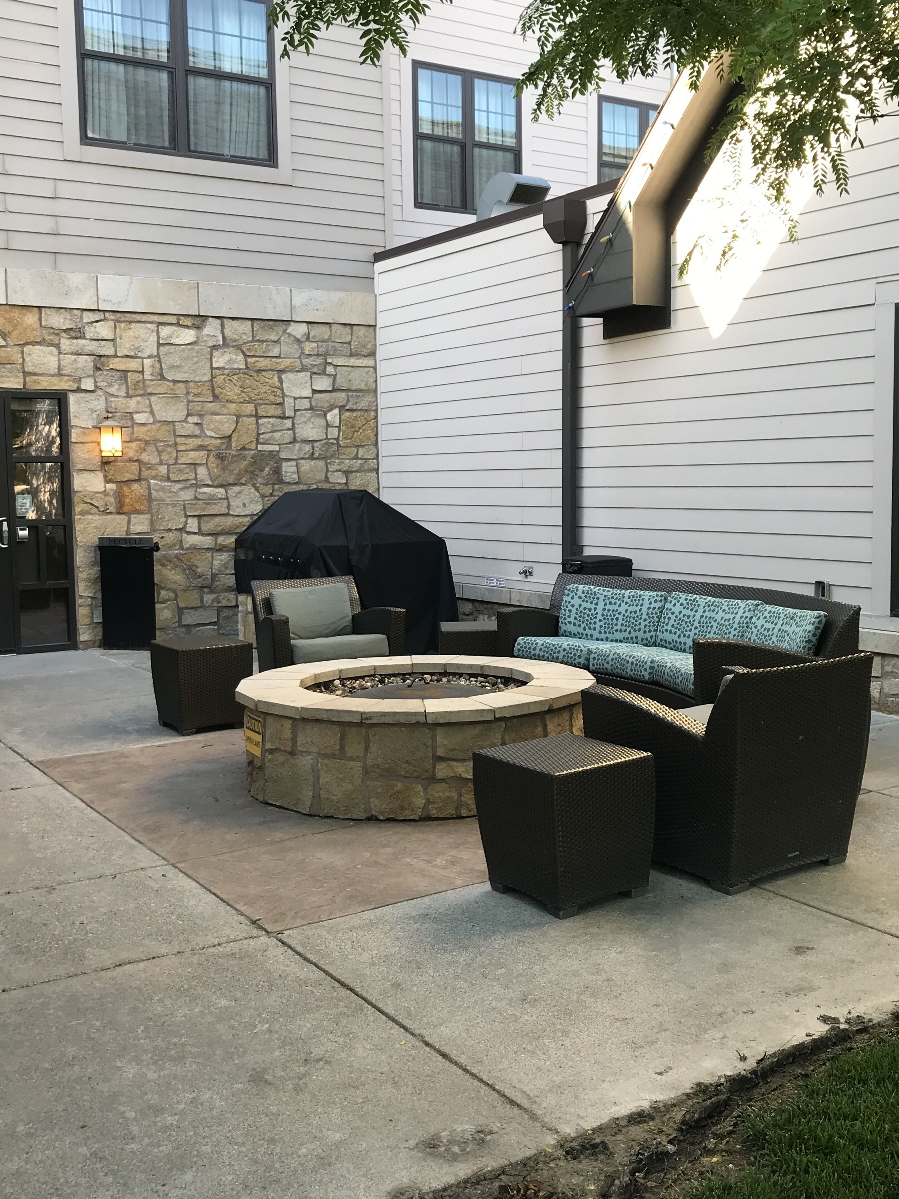 Une terrasse avec un mur en pierre, un foyer extérieur, du mobilier de jardin et un espace barbecue couvert.