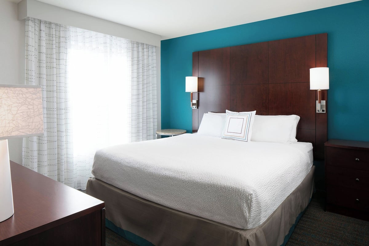 A hotel room with a large bed, two bedside lamps, a small round table, and a desk with a lamp.