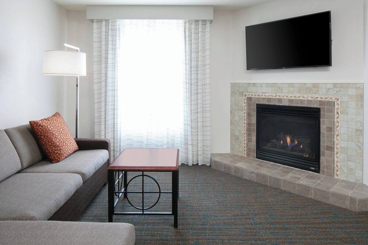 A living room with a sofa, a small table, a fireplace, and a TV mounted on the wall.