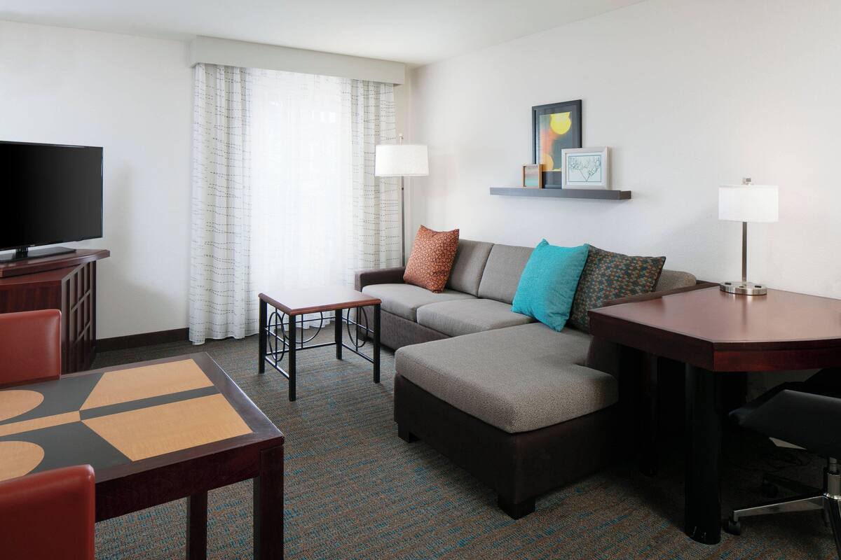 A hotel room with a sofa, ottoman, TV, table, chairs, and a lamp.