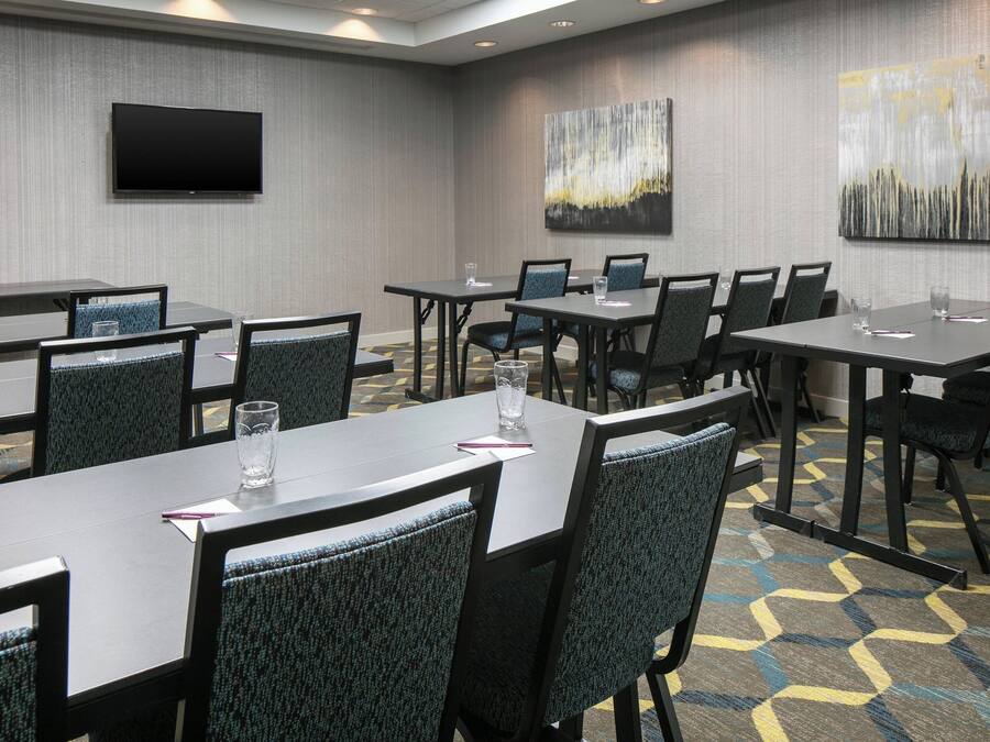 A conference room with multiple tables and chairs, a flat-screen TV mounted on the wall, and abstract paintings on the walls.