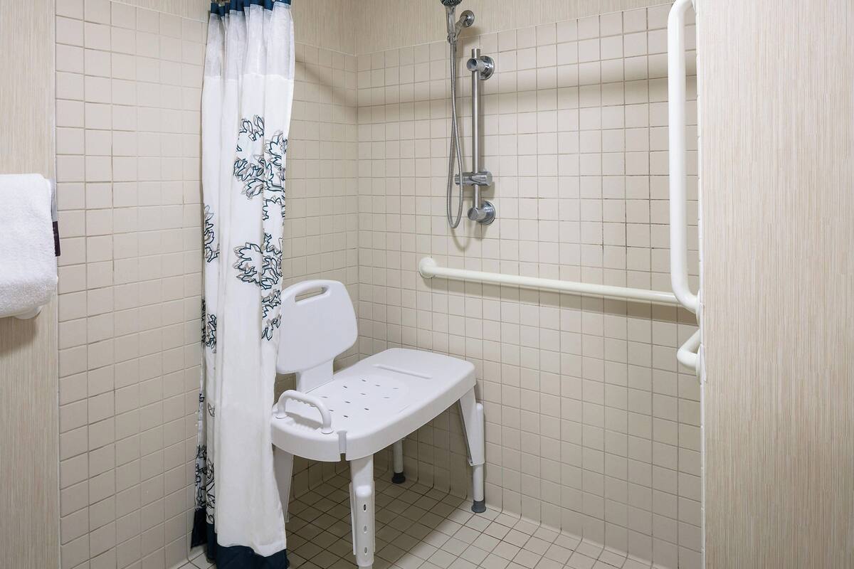 A small, tiled bathroom with a white toilet, a shower with a handheld showerhead, and a white grab bar.