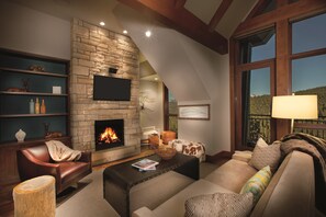 A cozy living room with a stone fireplace, leather sofas, and a large window offering a scenic view.