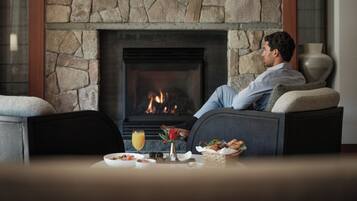 A man relaxing on a sofa by a stone fireplace with a glass of orange juice and a basket of food on the table.