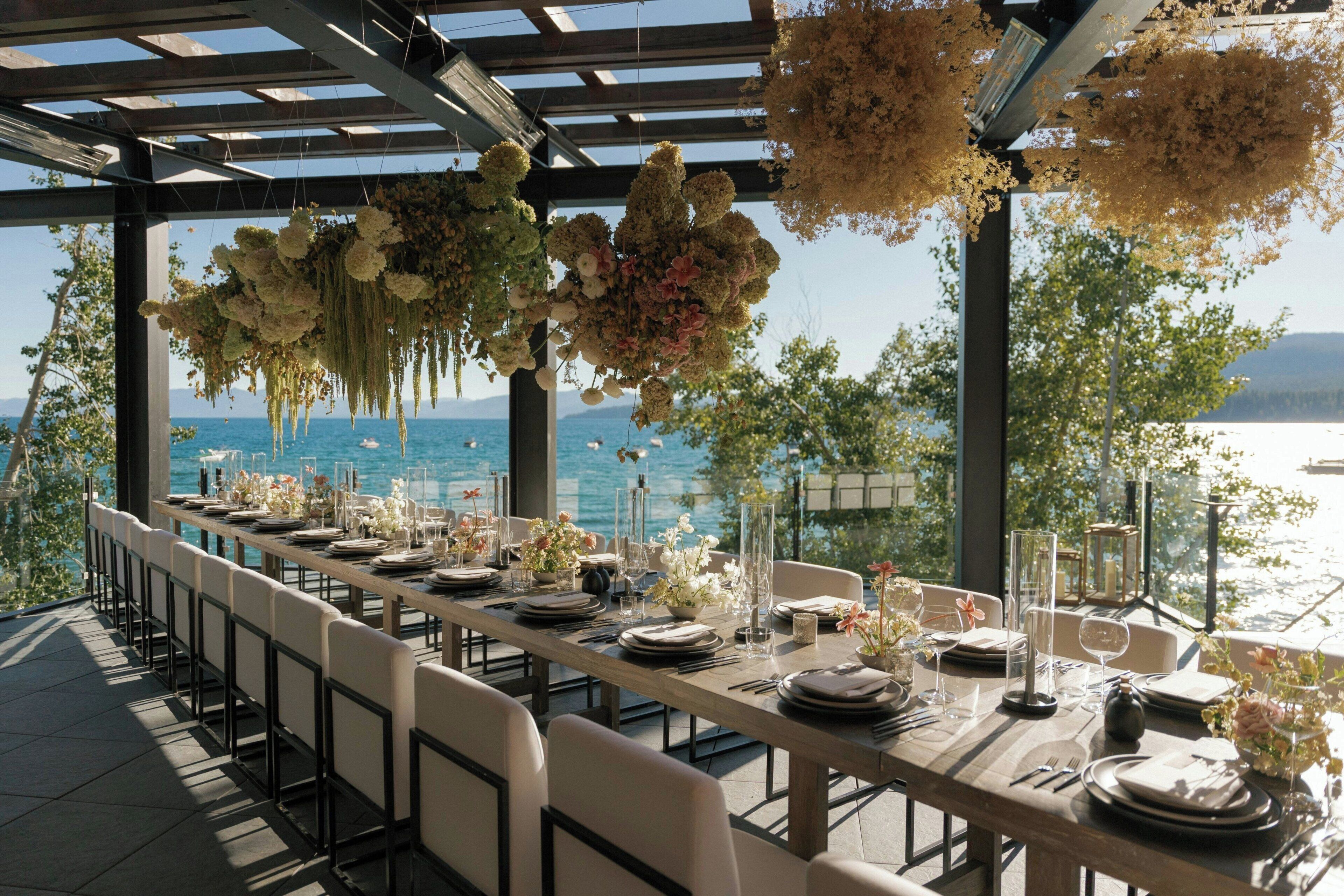 A long dining table set for a meal with a view of the sea.