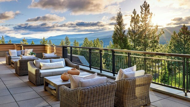A balcony with wicker furniture, a railing, and a view of mountains and trees. - The Ritz-Carlton, Lake Tahoe (Truckee)