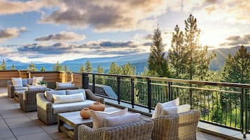A balcony with wicker furniture, a railing, and a view of mountains and trees.