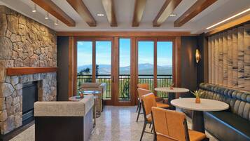 A spacious indoor area with a stone wall, a fireplace, a seating area with a sofa and chairs, and large windows offering a view of mountains.