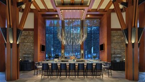 A spacious bar area with a long counter, multiple bar stools, and a large window offering a view of the outdoors. - The Ritz-Carlton, Lake Tahoe (Truckee)