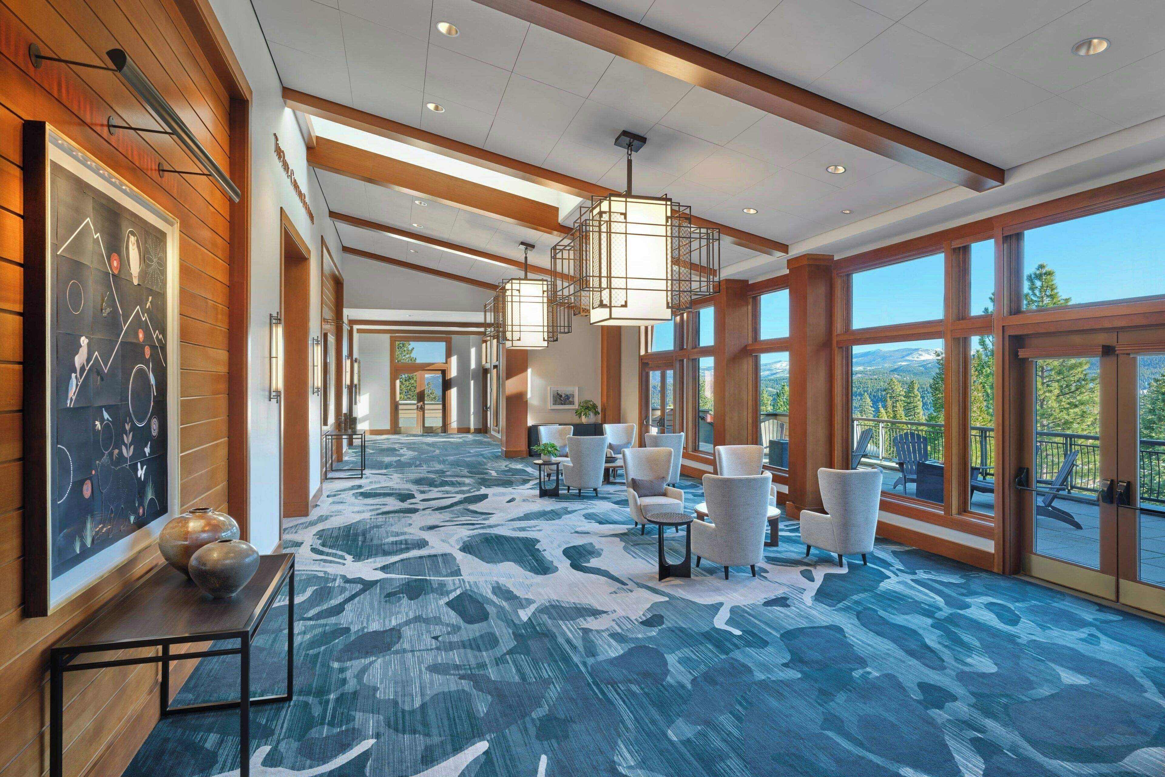 A spacious lobby with a patterned carpet, modern lighting fixtures, and large windows offering a view of the outdoors.