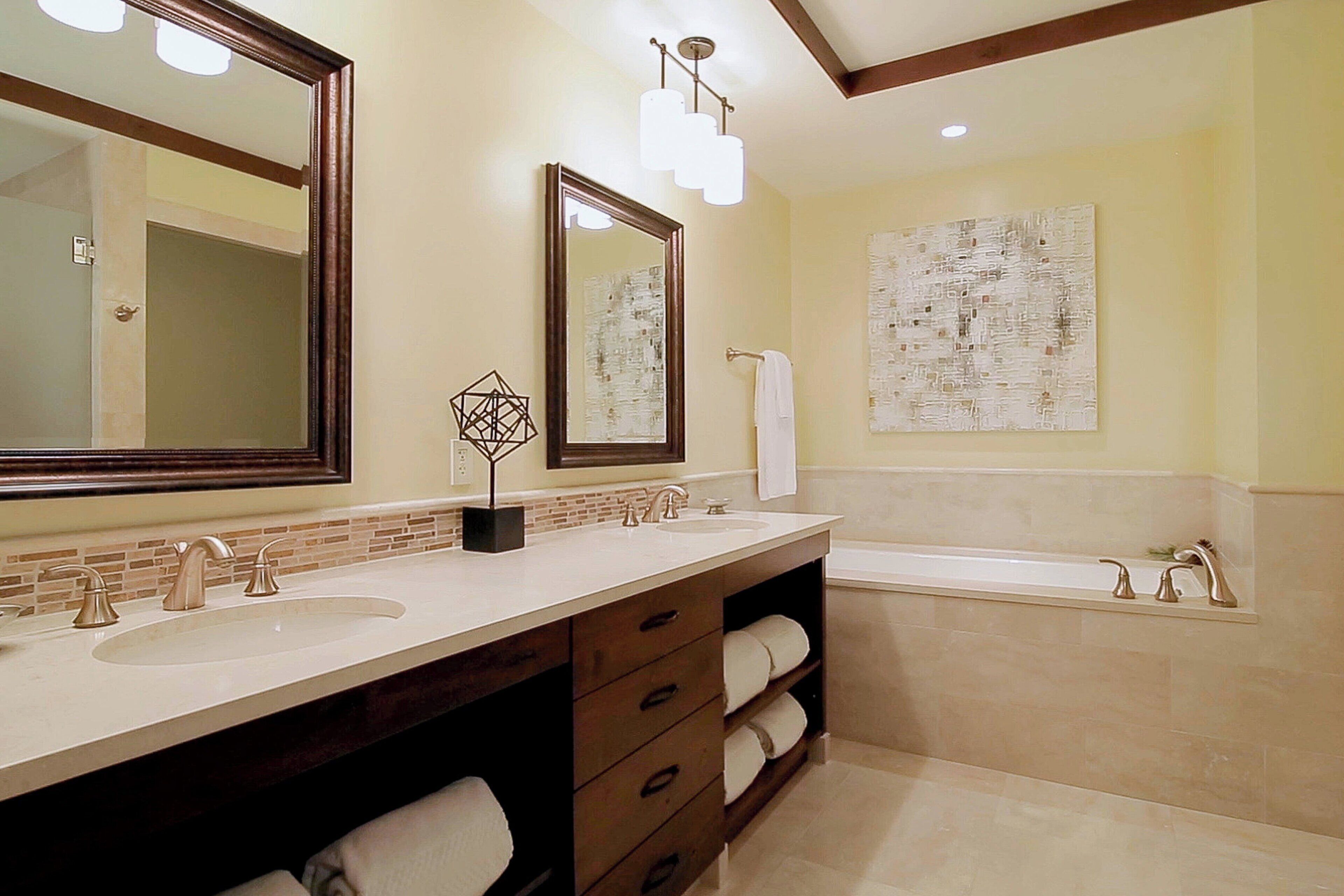 A modern bathroom with two sinks, a large mirror, a bathtub, and a towel rack.