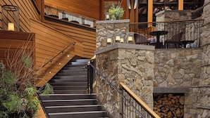 A grand staircase with wooden railings and stone walls, leading to a second-floor area with seating and a fireplace. - The Ritz-Carlton, Lake Tahoe (Truckee)