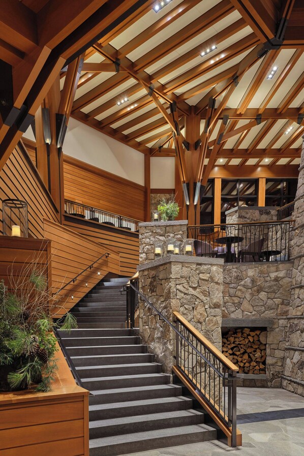 A grand staircase with wooden railings and stone walls, leading to a second-floor area with seating and a fireplace.
