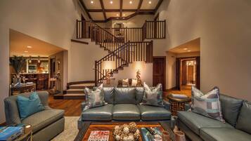 A spacious living room with a modern staircase, leather sofas, and a coffee table with magazines.