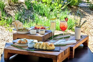 Mobiliario de comedor al aire libre con diversos platos, bebidas y una planta decorativa.