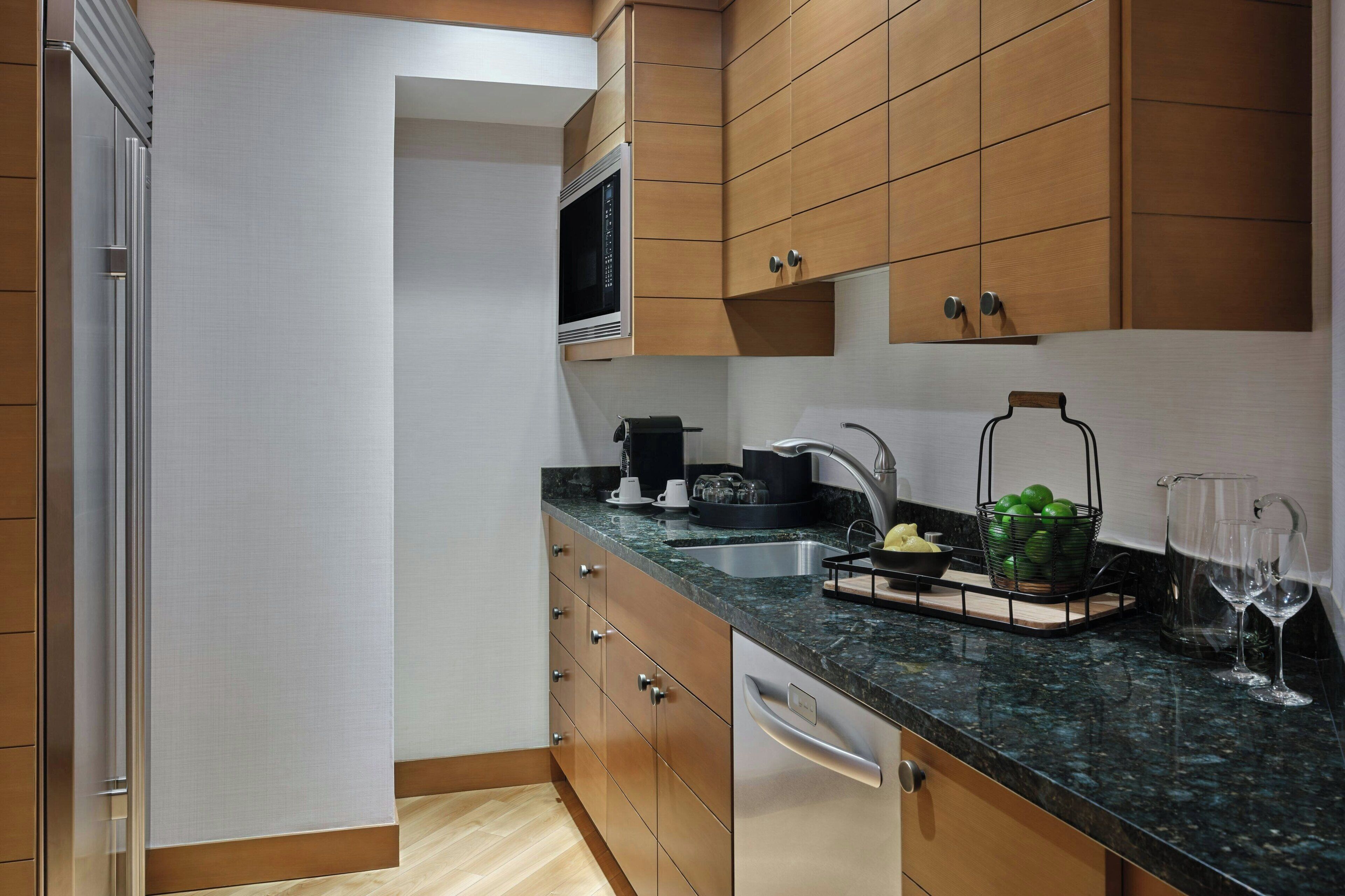 A modern kitchen with wooden cabinets, a stainless steel refrigerator, a microwave, and a sink.