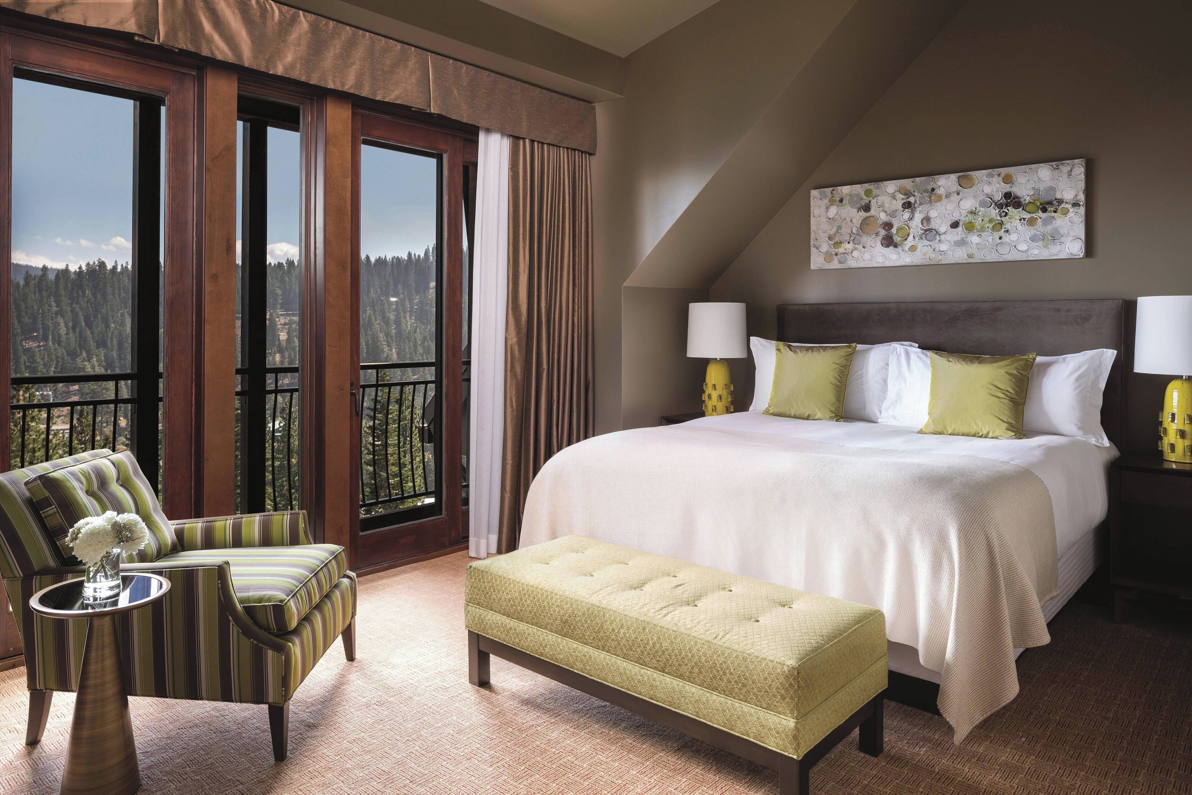 Ein Hotelzimmer mit einem großen Bett, einem Sessel, einer Bank und Blick ins Freie.