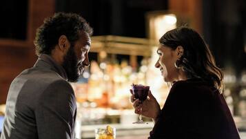 Um casal sentado em um bar, cada um com uma bebida na mão, uma garrafa de uísque e um copo de água no balcão.
