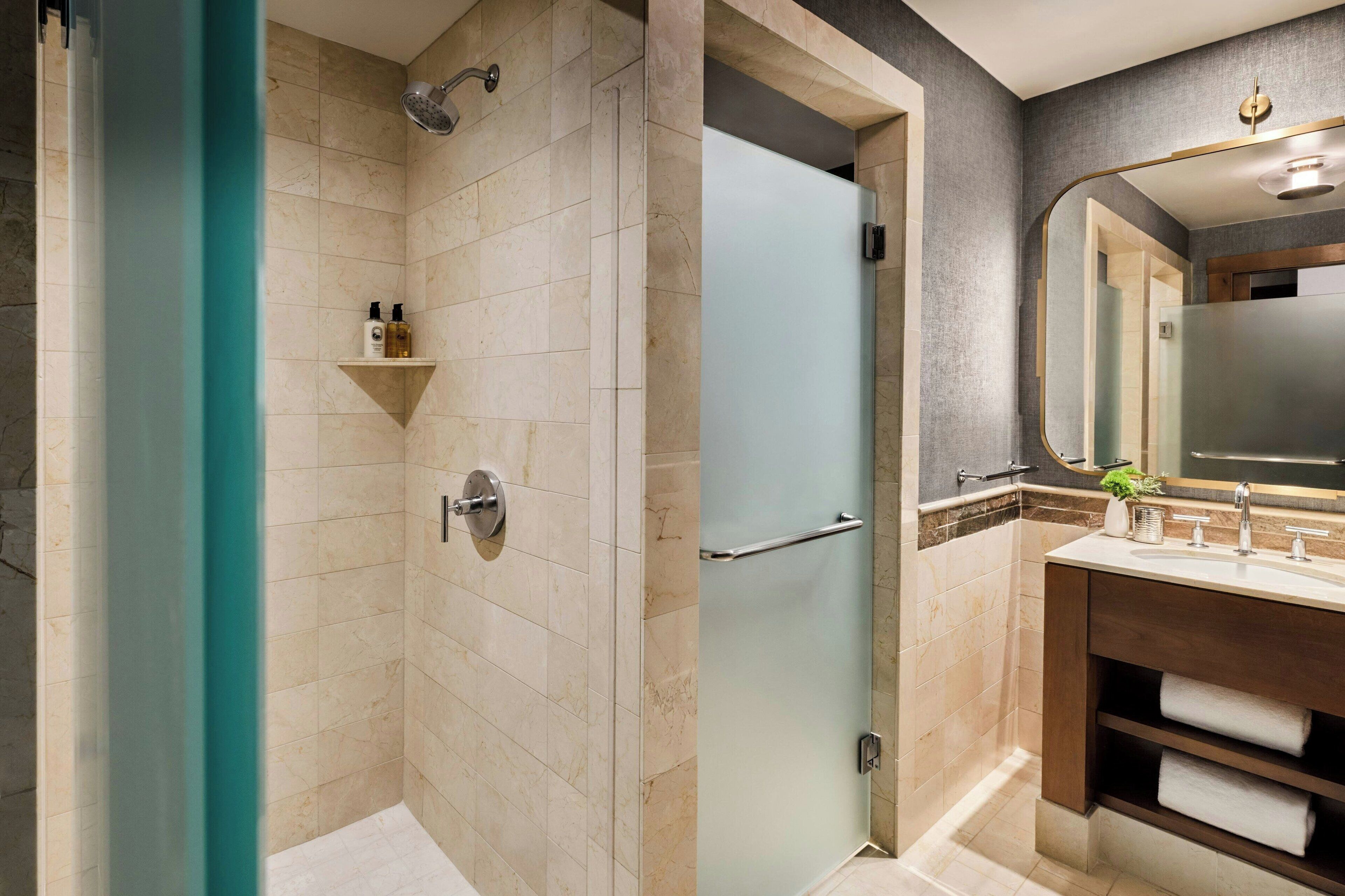 Une salle de bain moderne avec une douche à parois de verre, un meuble-lavabo avec miroir et une étagère contenant des articles de toilette.