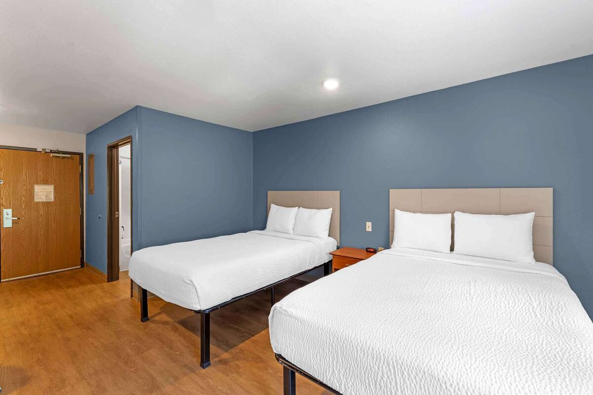 A hotel room with two single beds, wooden flooring, and a blue wall.
