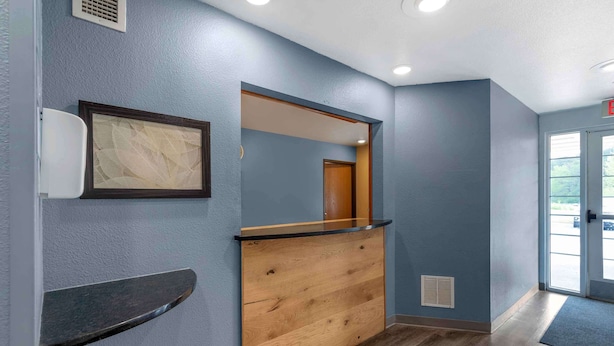 A reception area with a wooden counter, a framed artwork, and a door leading to the outside. - Extended Stay America Select Suites - Birmingham - Bessemer (Bessemer)