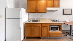 A compact kitchen with wooden cabinets, a white refrigerator, a sink, a stove, and a microwave. - Extended Stay America Select Suites - Birmingham - Bessemer (Bessemer)