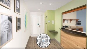 Un couloir avec un comptoir d’accueil, des œuvres d’art encadrées accrochées aux murs et un code QR sur le sol.