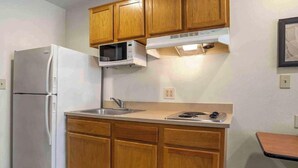 A compact kitchen with wooden cabinets, a white refrigerator, a microwave, a sink, and a stove. - Studio 6 Extended Stay Bossier City, LA - Shreveport (Bossier City)