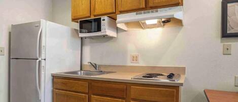 A compact kitchen with wooden cabinets, a white refrigerator, a microwave, a sink, and a stove.