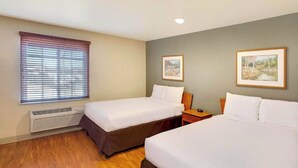A hotel room with two single beds, a heater, a window with blinds, and two framed pictures on the wall. - Studio 6 Extended Stay Bossier City, LA - Shreveport (Bossier City)