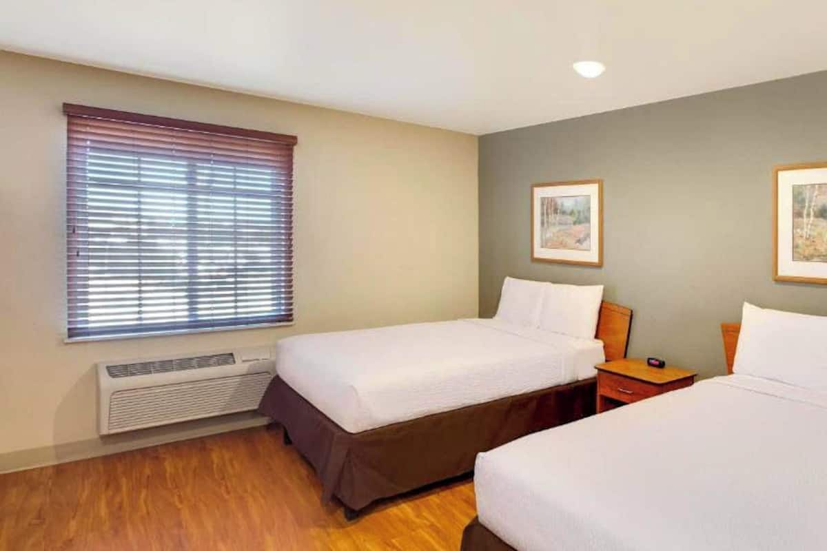 Una habitación de hotel con dos camas individuales, un calentador, una ventana con persianas y dos cuadros en la pared.