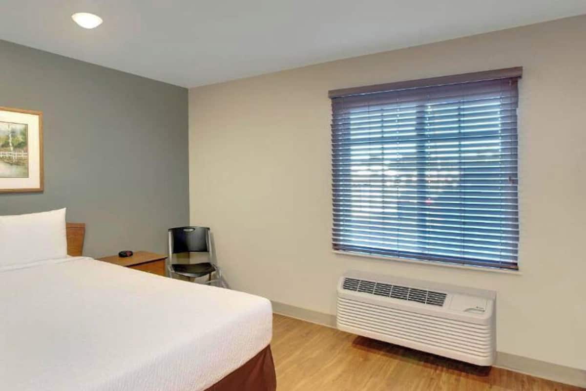 Una habitación de hotel con cama, una silla, un calentador y una ventana con persianas.