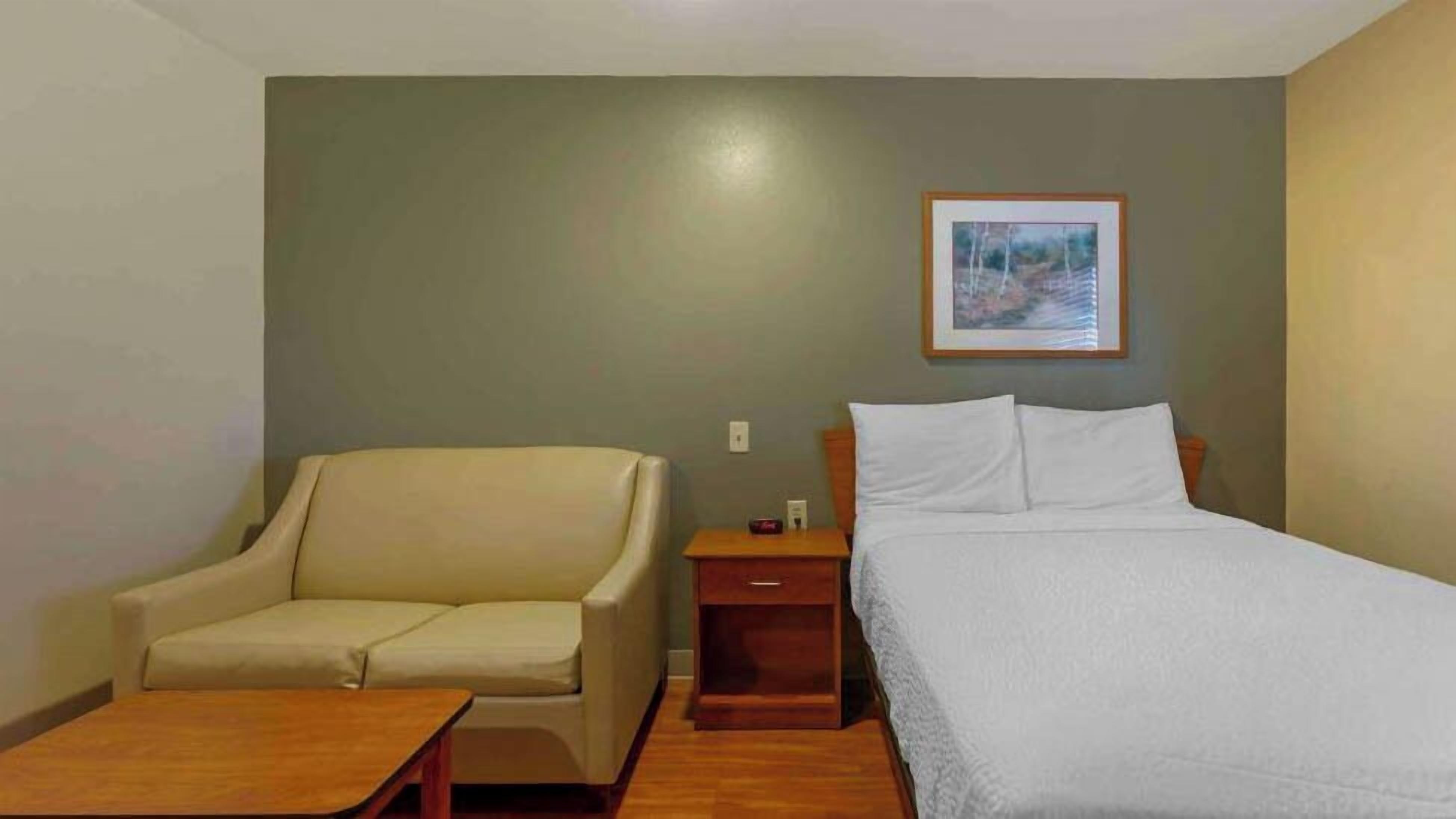 Une chambre d’hôtel avec un lit, une chaise, une petite table et une table de chevet avec une lampe.