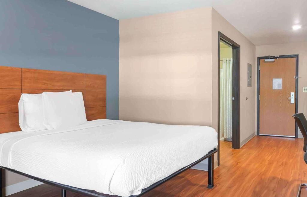 A hotel room with a bed, a wooden headboard, a door, and a wall with a light switch.