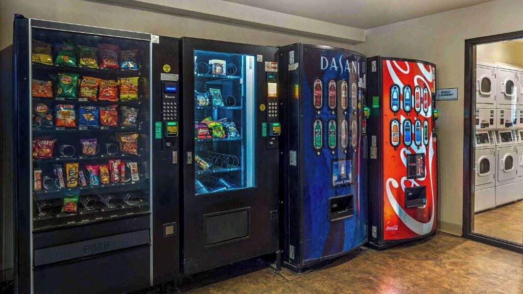 Quatre distributeurs automatiques alignés, dont l’un vend du Coca-Cola et l’autre de l’eau Dasani.