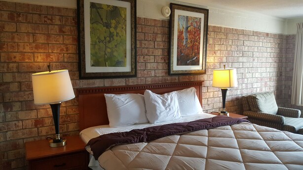 A hotel room with a brick wall, a large bed with white bedding, two framed artworks, and two bedside lamps. - Budget Host Platte Valley Inn (Julesburg)