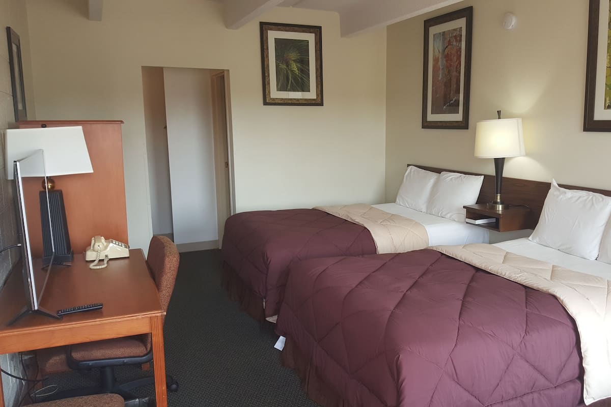 A hotel room with two beds, a desk with a telephone, a chair, and a lamp.