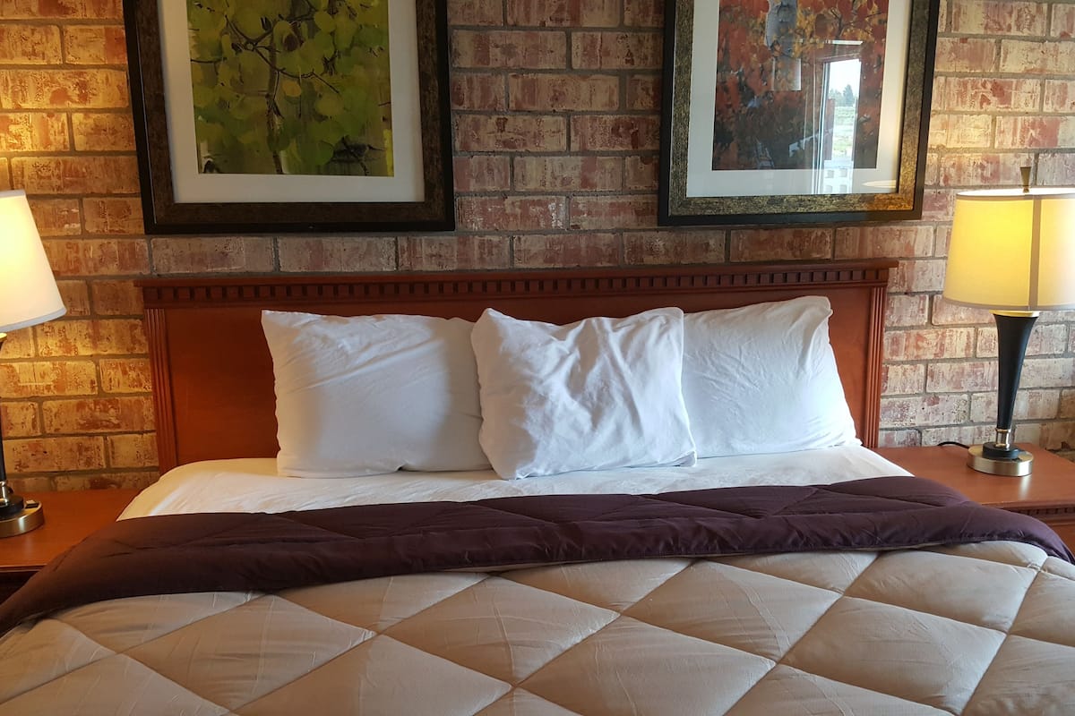 A hotel room with a wooden headboard, two white pillows, a quilted bedspread, and two bedside lamps.