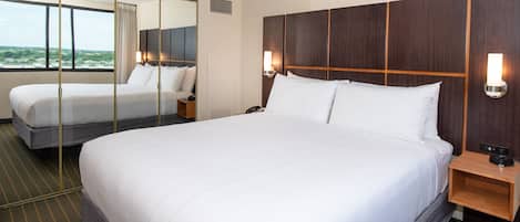 A hotel room with a large bed, a bedside table with a lamp, a mirror, and a view of the outdoors.