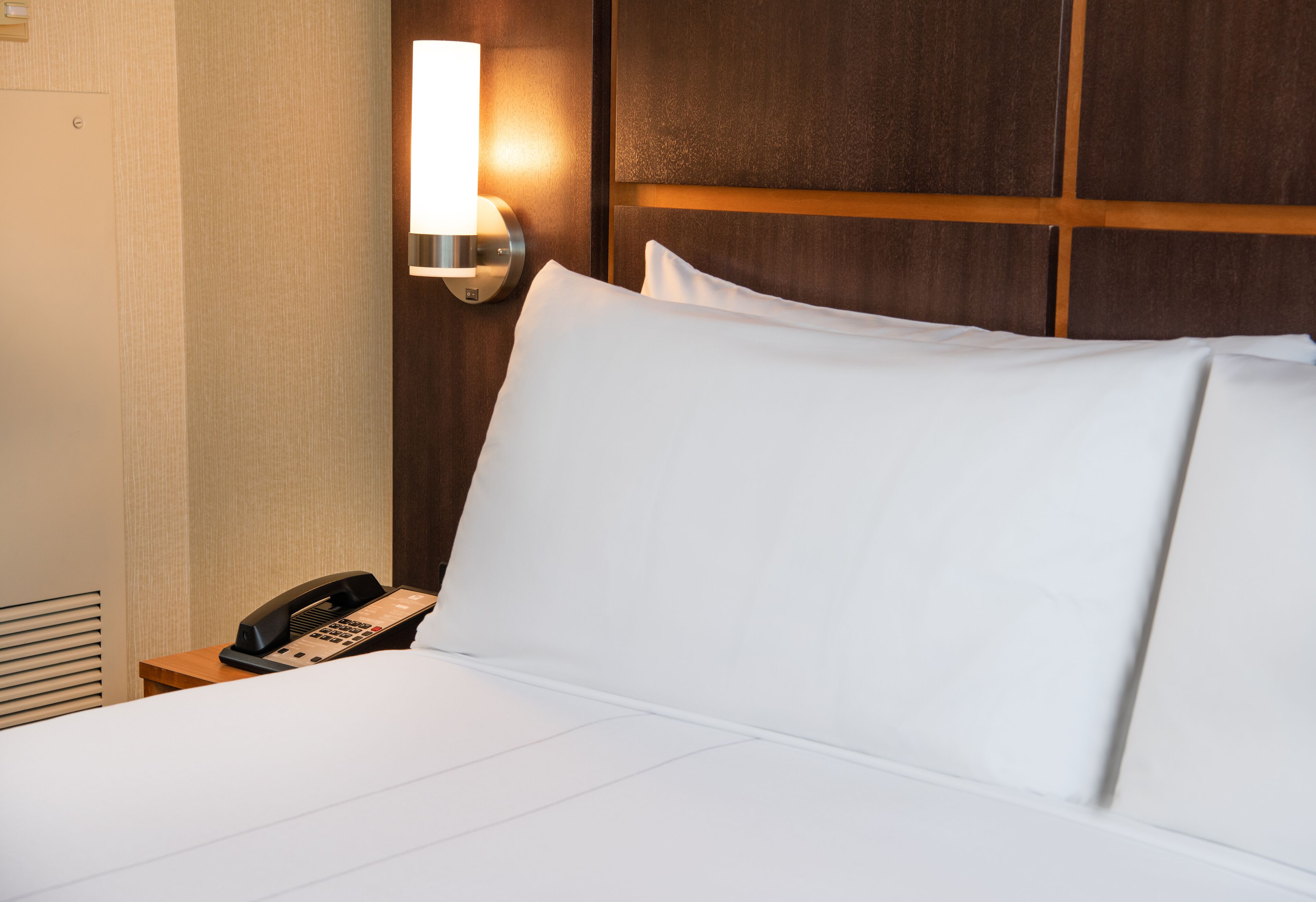 A hotel room with a bed, a bedside telephone, and a wall-mounted light fixture.