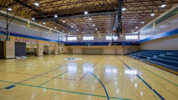 Una cancha de baloncesto cubierta con techo alto, múltiples aros y un letrero que dice 'PLAY SMART, PLAYSAFE'.